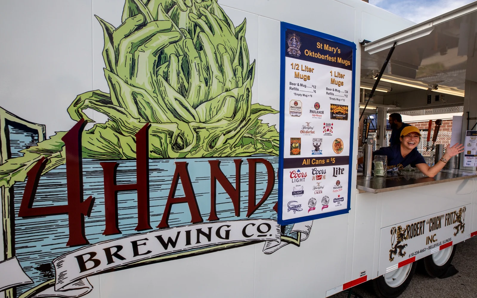 Beer trailer service window with Oktoberfest mug signage and a volunteer serving guests